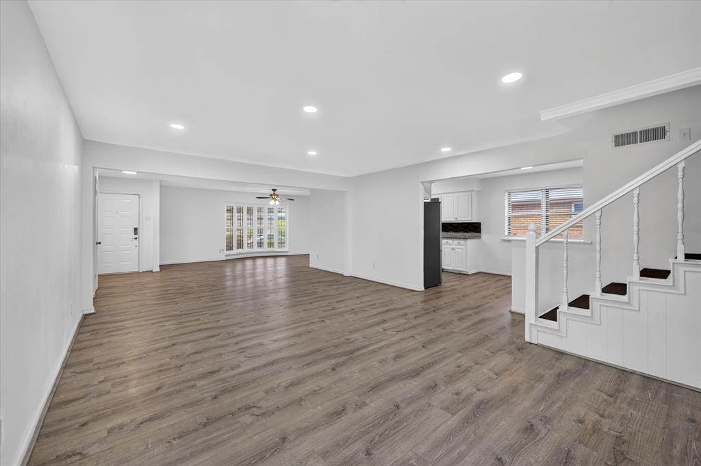 Open-concept interior featuring wood-finish flooring, recessed lighting, a multi-pane bay window, and a staircase with painted wood railings Open-concept interior featuring wood-finish flooring, recessed lighting, a multi-pane bay window, and a staircase with painted wood railings