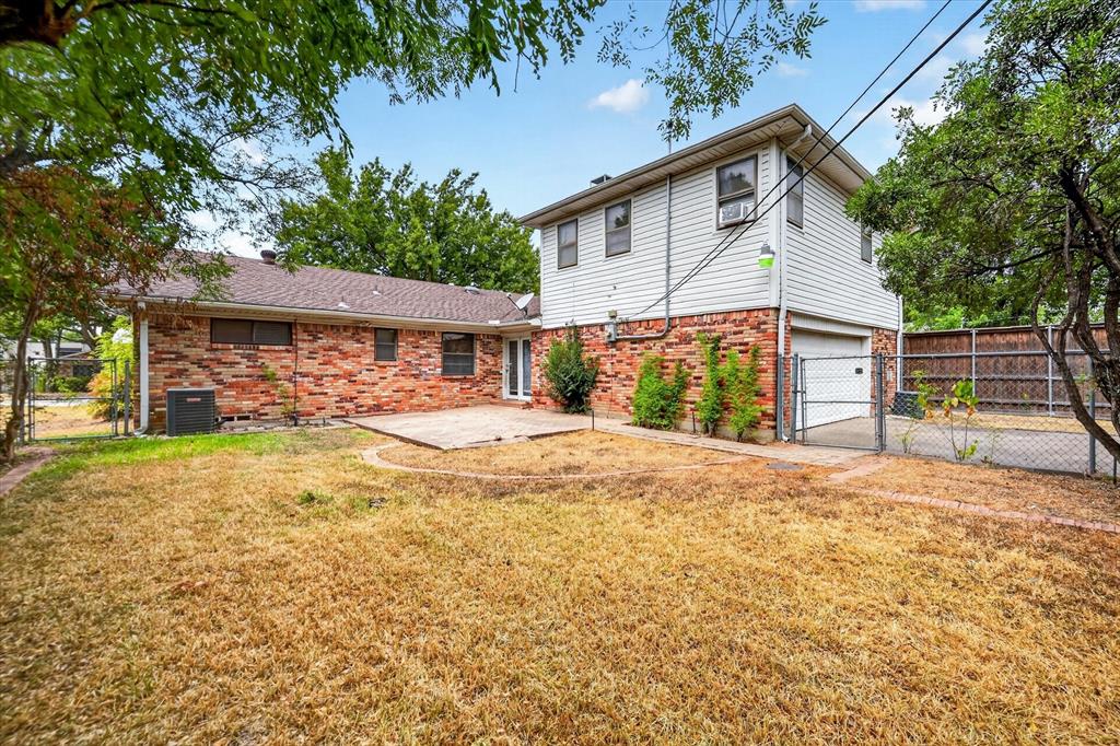 Two-story exterior featuring multi-toned brick and horizontal siding, stone patio, attached garage, and metal chain-link fencing