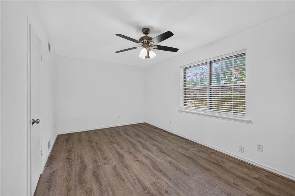 Neutral interior featuring wood-finish flooring, a multi-blade ceiling fan with integrated lighting, and a window with horizontal blinds