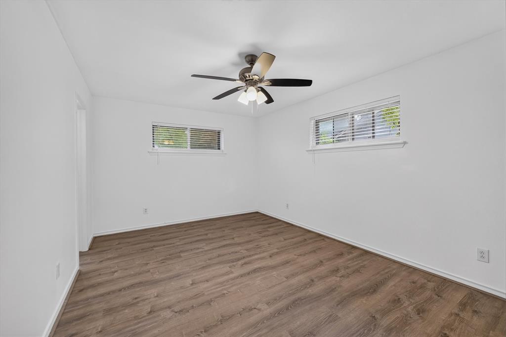 Room featuring wood-finish flooring, white walls, dual windows with blinds, and a central ceiling fan with integrated lighting