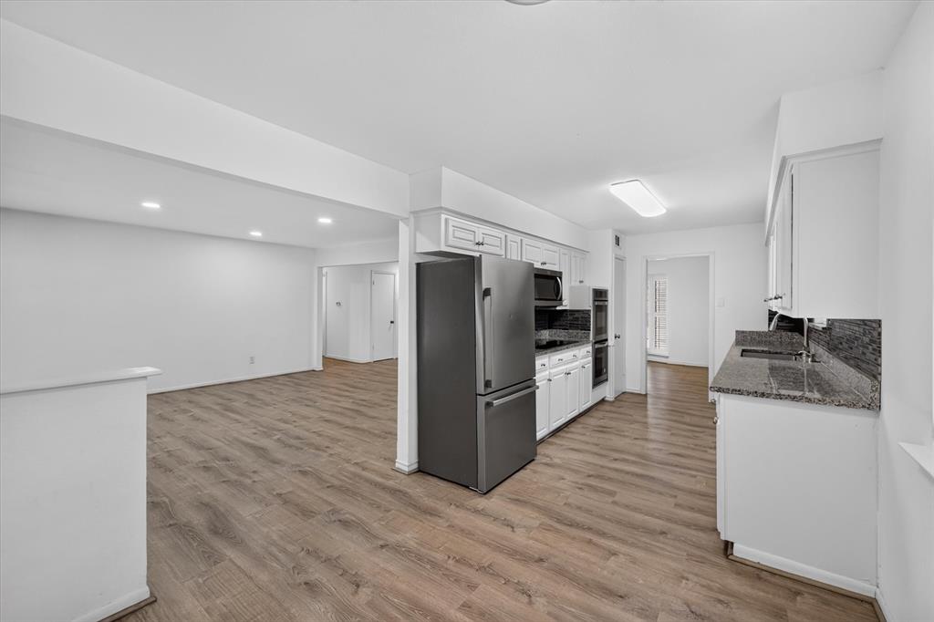 Kitchen featuring white cabinetry, stone-finish countertops, stainless steel refrigerator, and built-in double wall oven, finished with wood-finish flooring Kitchen featuring white cabinetry, stone-finish countertops, stainless steel refrigerator, and built-in double wall oven, finished with wood-finish flooring