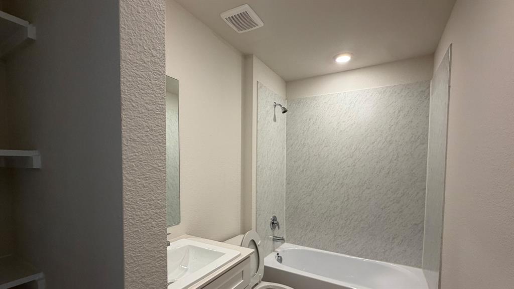 White tub and shower combination with textured wall surround, chrome fixtures, and recessed lighting