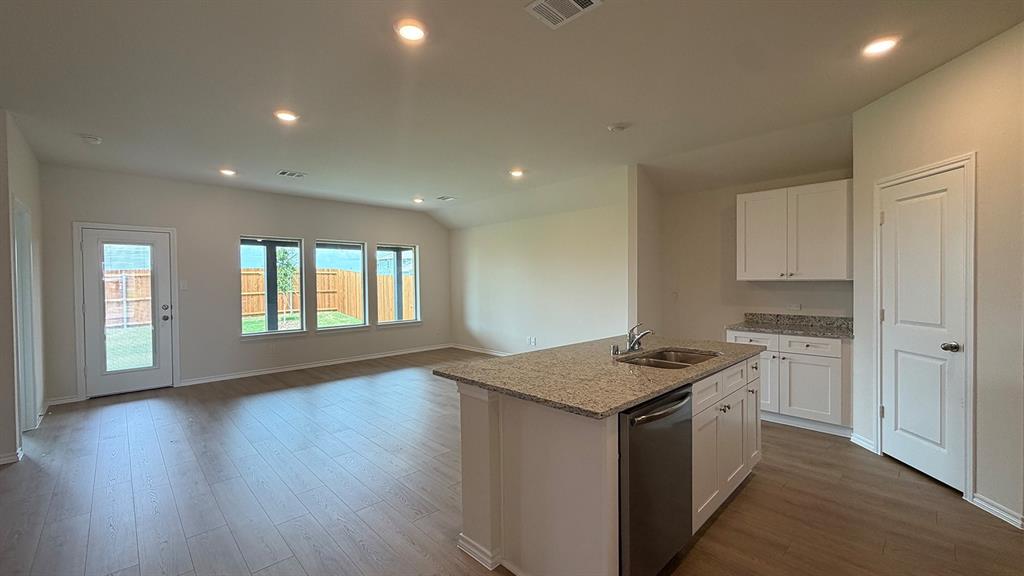 Open-concept living area featuring wood-finish flooring, recessed lighting, and a kitchen island with a double basin sink and stainless steel dishwasher