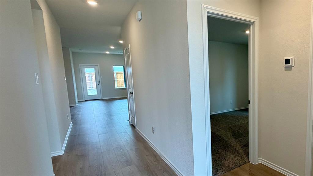 Hallway with wood-finish flooring, recessed lighting, and a white interior door leading to a room with dark carpeting
