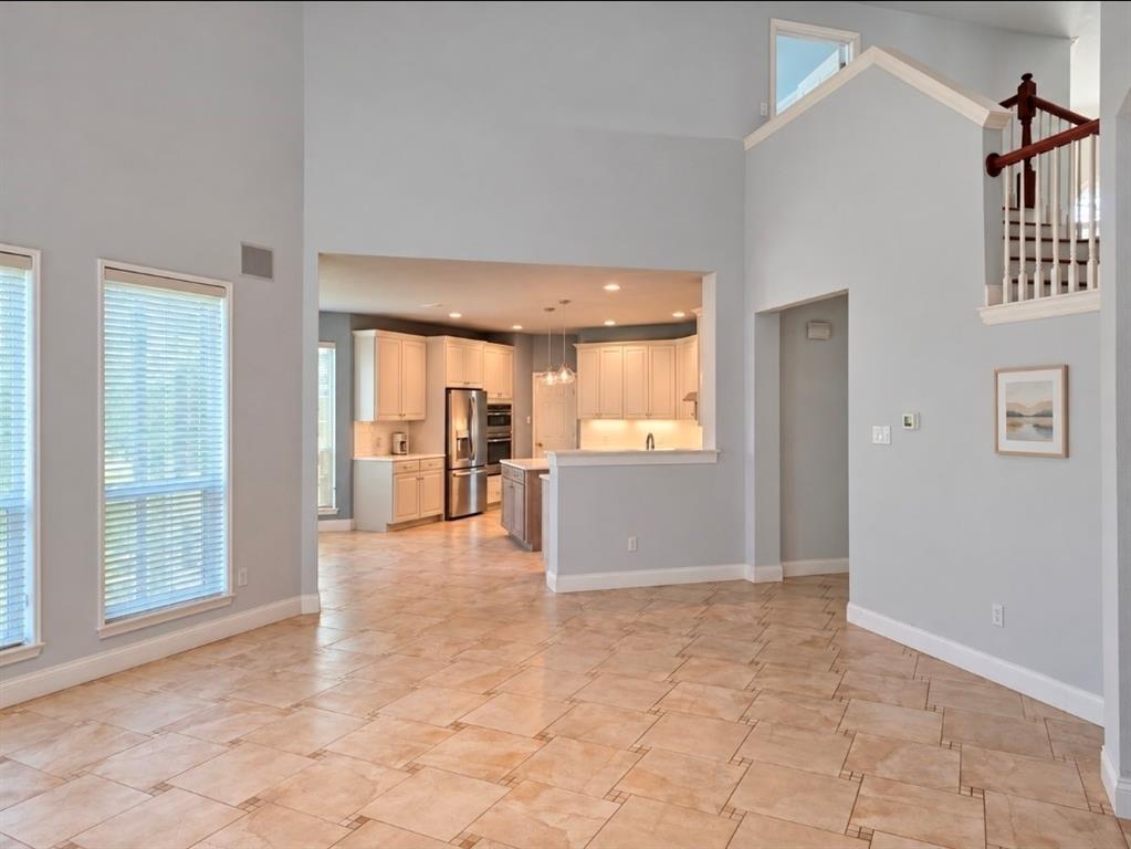 High-ceiling interior featuring tile flooring, a staircase with a wooden handrail, and a kitchen equipped with cabinetry and stainless steel appliances High-ceiling interior featuring tile flooring, a staircase with a wooden handrail, and a kitchen equipped with cabinetry and stainless steel appliances