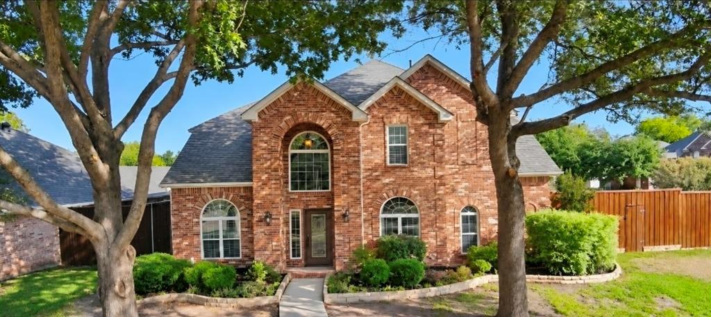 Two-story brick exterior featuring an arched entryway, decorative stone-edged landscaping, and a multi-gabled roofline Two-story brick exterior featuring an arched entryway, decorative stone-edged landscaping, and a multi-gabled roofline