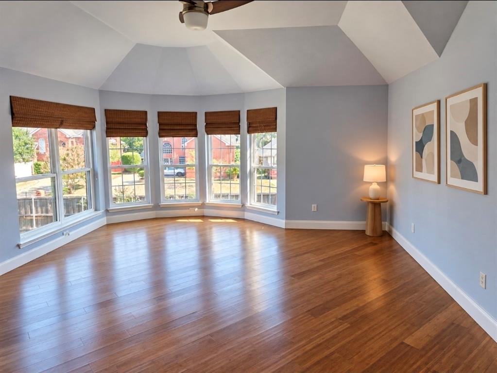 Vaulted ceiling with a centrally mounted ceiling fan, multi-window bay configuration, and wood-finish flooring