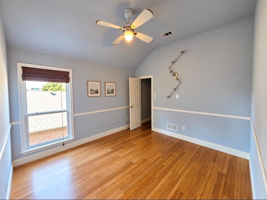 Room featuring wood-finish flooring, vaulted ceilings, chair rail molding, a white ceiling fan with integrated lighting, and wall-mounted track lighting
