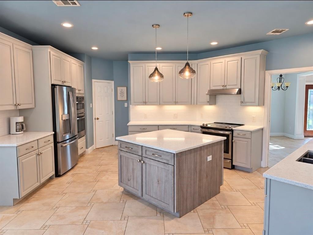 Kitchen featuring a central island with wood-finish cabinetry, quartz countertops, tile flooring, stainless steel appliances, and pendant lighting Kitchen featuring a central island with wood-finish cabinetry, quartz countertops, tile flooring, stainless steel appliances, and pendant lighting