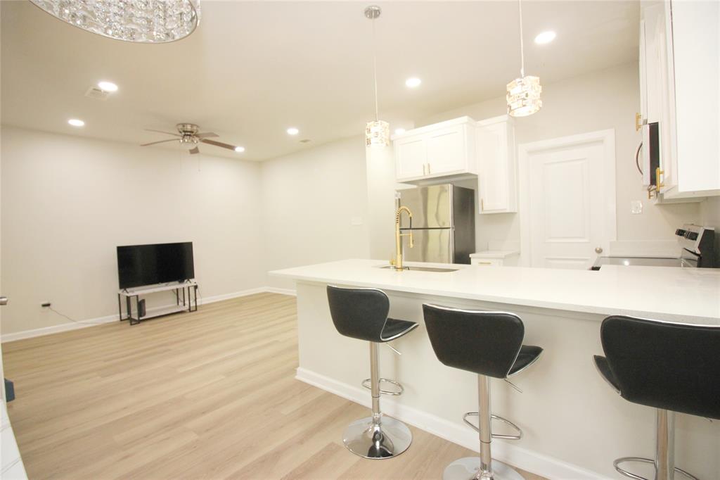Kitchen featuring a quartz countertop island with a brass faucet, white shaker-style cabinetry, stainless steel appliances, pendant lighting, and wood-finish flooring