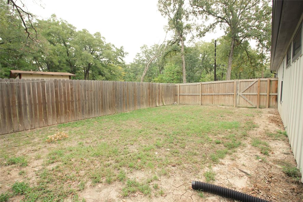 Rear yard enclosed by a tall wood privacy fence with a gated entry, featuring mature trees and vertical siding on the exterior wall