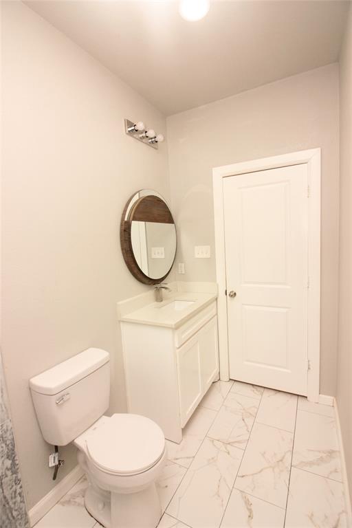 Bathroom featuring a white vanity with a neutral countertop, circular wall-mounted mirror, three-light fixture, and large-format tile flooring
