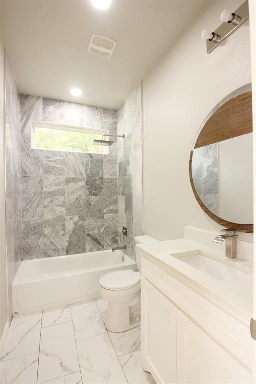 Bathroom featuring natural stone tile shower surround, porcelain floor tile, white vanity cabinet with quartz countertop, and a circular wood-trimmed mirror