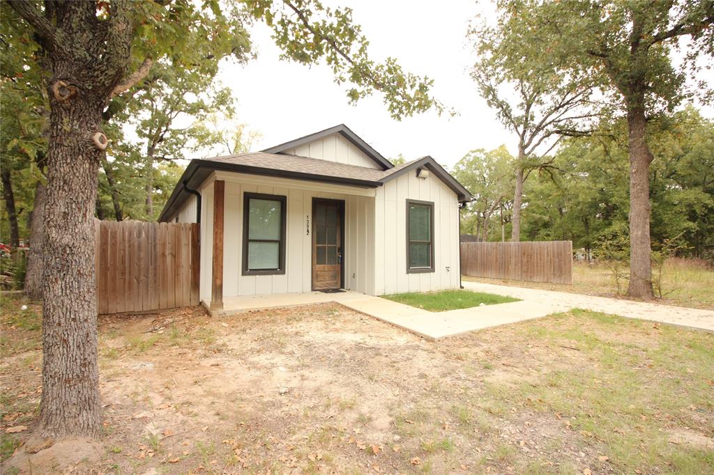 Exterior featuring board-and-batten siding, a covered entryway with a wood post, vertical windows with dark trim, and a concrete walkway Exterior featuring board-and-batten siding, a covered entryway with a wood post, vertical windows with dark trim, and a concrete walkway