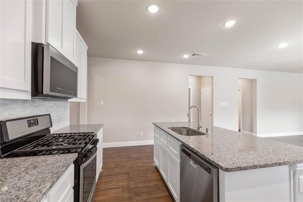 Kitchen featuring white cabinetry, stone countertops, stainless steel appliances, a center island with a built-in sink, and wood-finish flooring