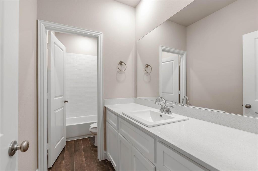 Bathroom featuring a single-sink vanity with a quartz countertop, white shaker-style cabinetry, a large wall-mounted mirror, and wood-finish flooring