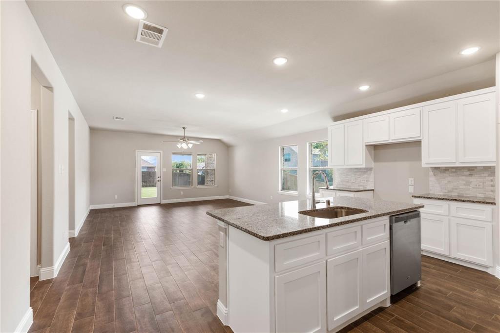 Kitchen featuring a central island with stone countertop, stainless steel dishwasher, white cabinetry, tile backsplash, and wood-finish flooring