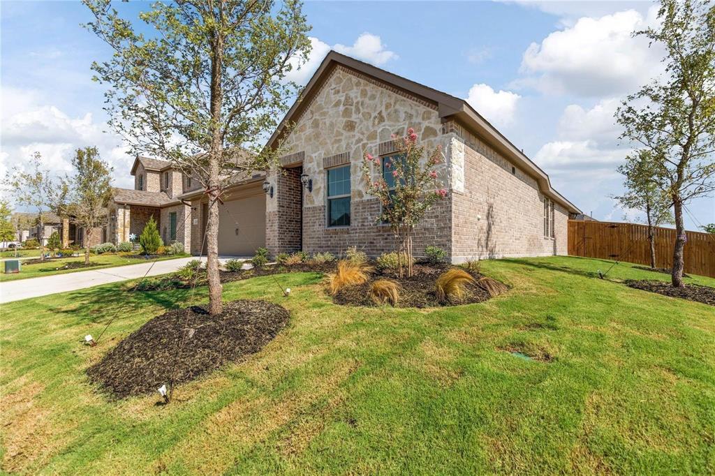 Single-story residence featuring a combination stone and brick facade, gabled roofline, attached multi-car garage, and landscaped front lawn with mulch beds