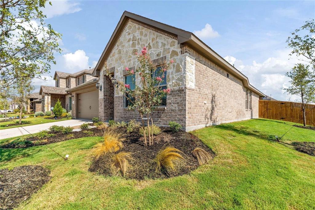 Single-story exterior featuring a combination of brick and stone veneer, a gable roofline, an attached multi-car garage, and landscaped front lawn with mulch beds