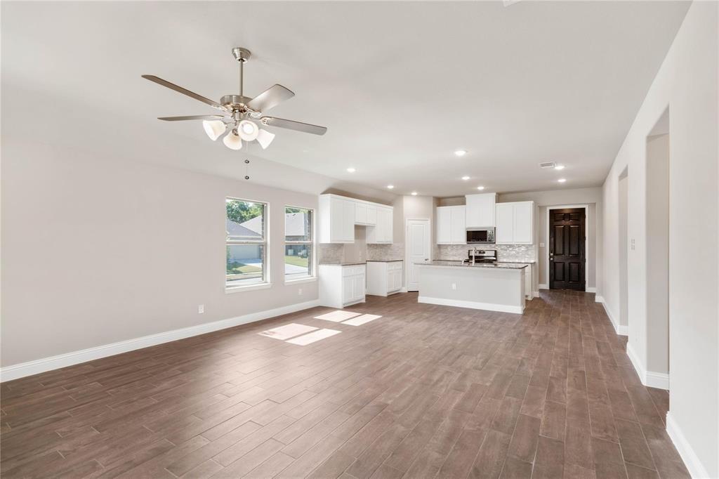 Open-concept interior featuring wood-finish flooring, recessed lighting, and a kitchen equipped with white cabinetry, a center island, and built-in appliances