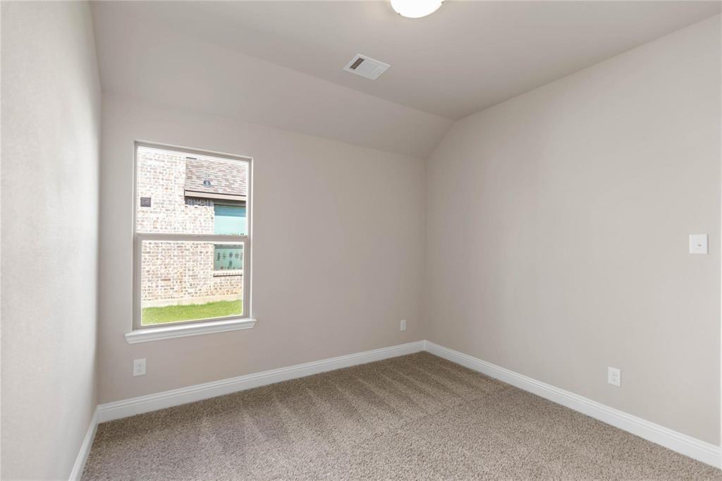 Neutral-toned interior room featuring wall-to-wall carpeting, vaulted ceilings, and a single window with a view of a brick exterior