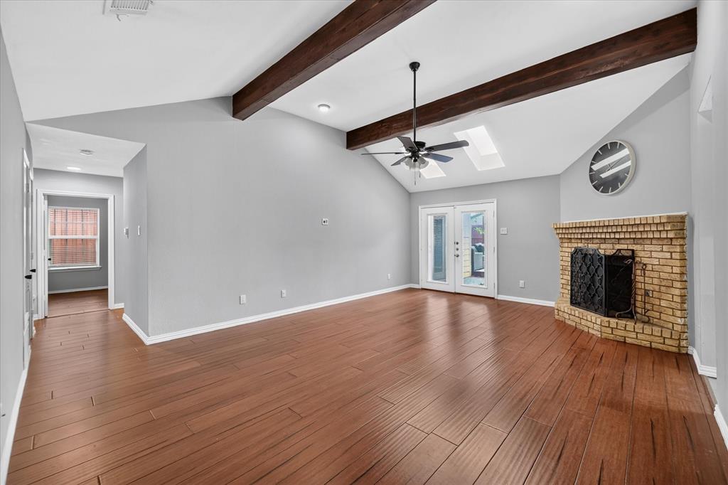 Vaulted ceiling featuring exposed wood beams, wood-finish flooring, brick fireplace, skylights, and double-glass doors