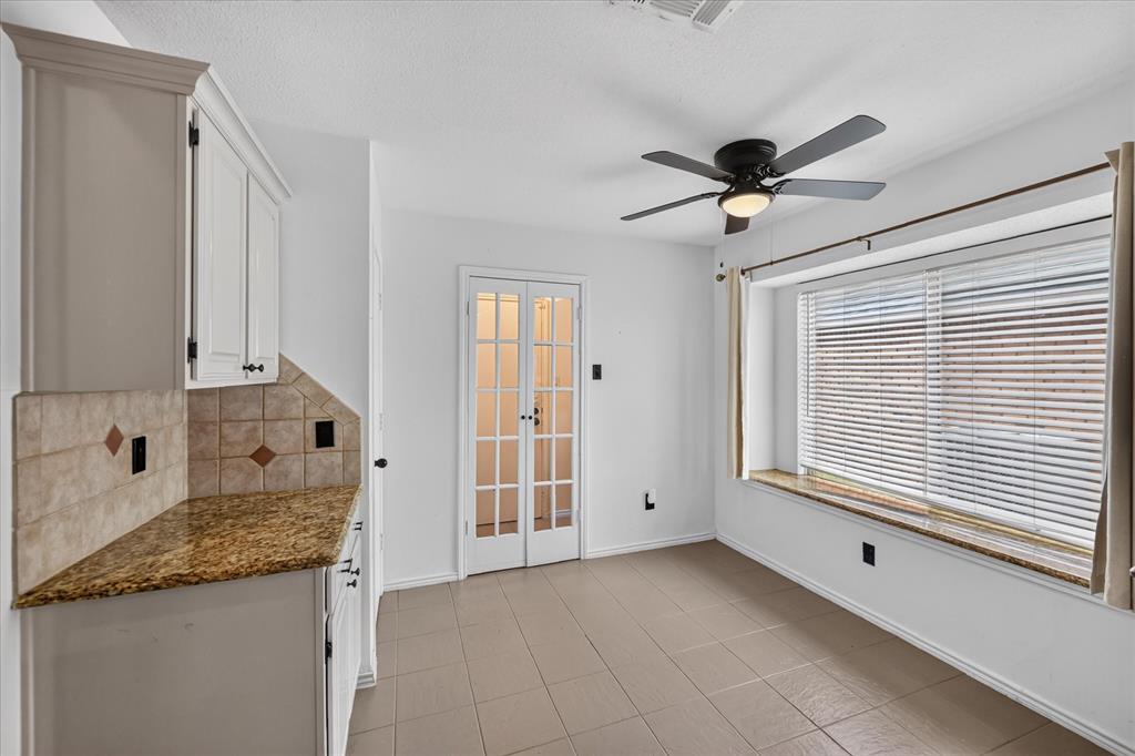 White cabinetry, stone-finish countertops, tile backsplash, built-in window seat, and multi-pane French doors