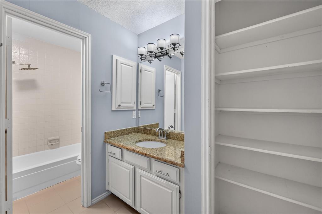 Bathroom featuring a stone-surface vanity with an integrated undermount sink, multi-light fixture, built-in shelving unit, and a tiled tub-shower combination