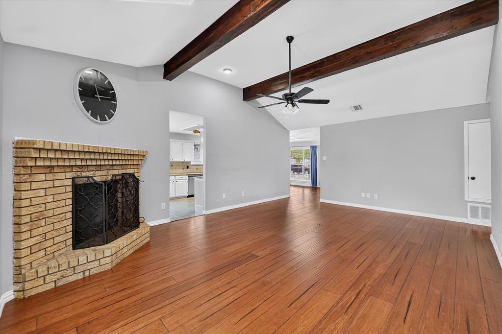 Vaulted ceilings featuring exposed wood beams, wood-finish flooring, and a brick fireplace
