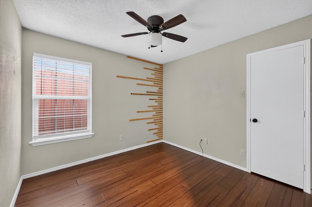 Interior room featuring wood-finish flooring, a ceiling fan with integrated lighting, a single-hung window with blinds, and decorative wood-slat wall paneling