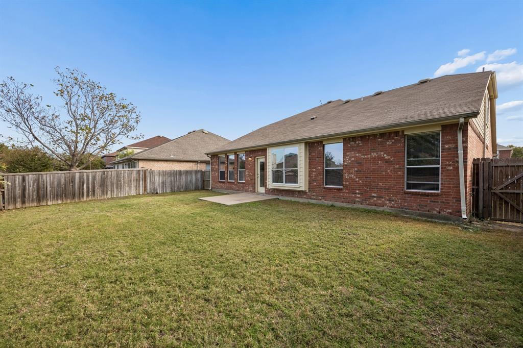 The home's rear exterior showcases classic red brick construction accented by light-colored trim and multiple windows. A fully fenced backyard offers a private outdoor setting with an open lawn and a concrete patio just off the back of the home. With room to enjoy outdoor activities, gardening, or casual gatherings, this backyard offers a wonderful opportunity to create a personalized outdoor retreat.