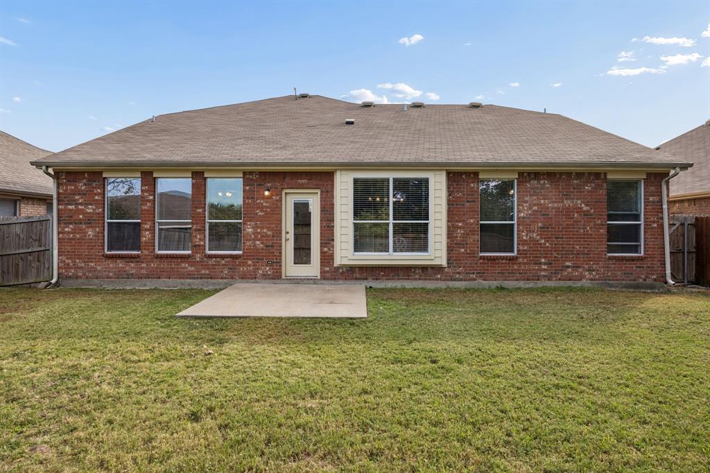 A full view of the home's rear elevation highlights the traditional brick exterior, complementary siding accents, and well-positioned windows that bring natural light into the interior. The fenced backyard features an open grassy lawn and a concrete patio, providing a functional outdoor space with potential for relaxing, entertaining, or creating a garden area.