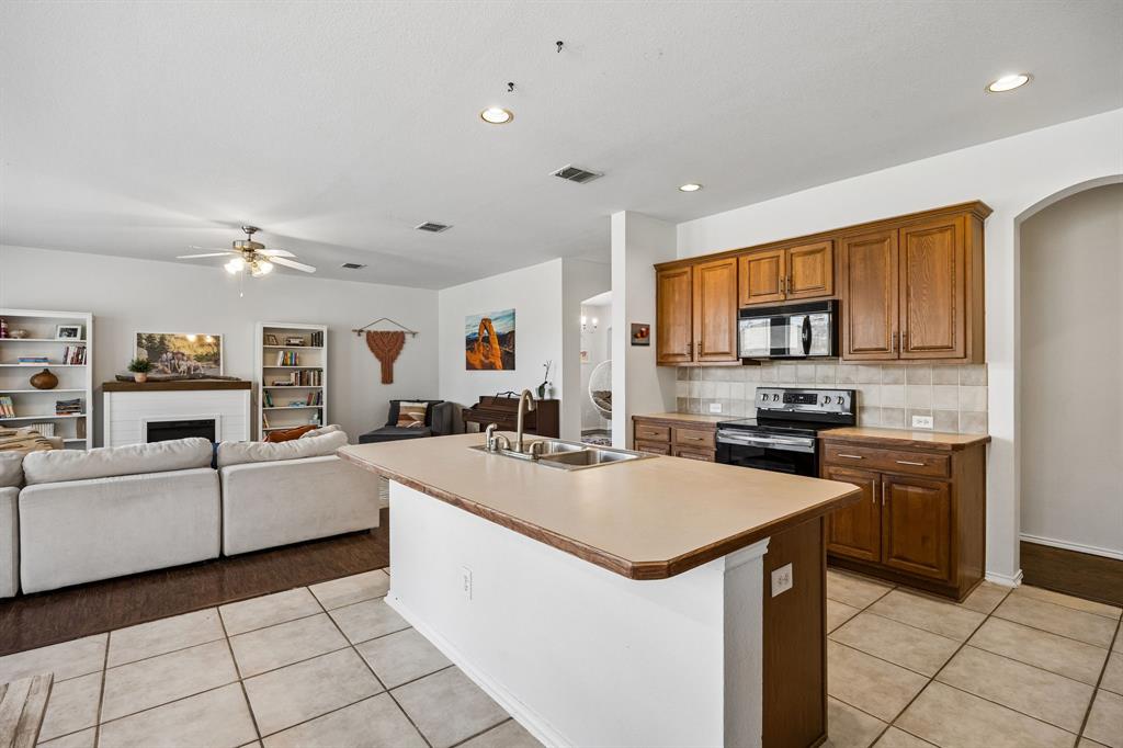 The kitchen showcases rich wood cabinetry, a complementary tile backsplash, and generous counter space for everyday meal preparation. A spacious center island with a built-in sink provides additional workspace and creates a natural gathering point. Recessed lighting brightens the space, while the open-concept layout flows seamlessly into the living area, creating an inviting atmosphere for entertaining and everyday living.