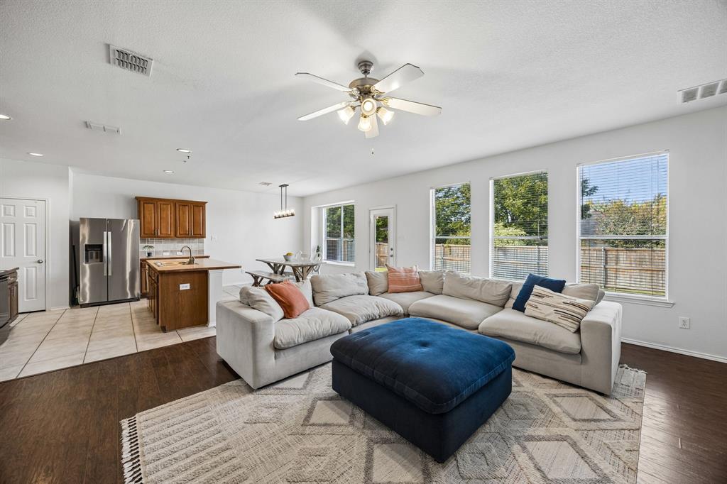Spacious and welcoming, the living room features beautiful dark wood flooring, abundant natural light, and a soft, neutral color palette that creates an airy, comfortable atmosphere. Three large windows bring the outdoors in, while a charming fireplace framed by built-in shelving creates an attractive focal point. The generous layout offers plenty of room for relaxing, gathering, and entertaining.