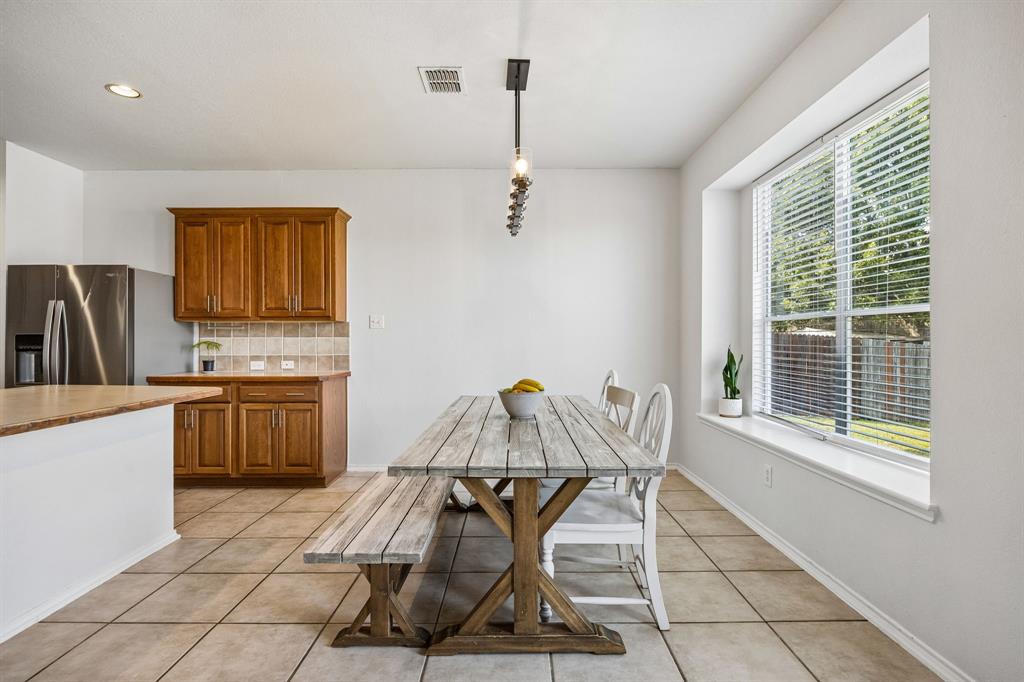 The dining area is filled with natural light from a generously sized window overlooking the backyard, creating a bright and cheerful setting for everyday meals and special gatherings. Neutral tile flooring offers durability and easy maintenance, while the adjoining kitchen provides convenient access to the main living spaces. A contemporary pendant light adds a refined finishing touch to this welcoming dining nook.