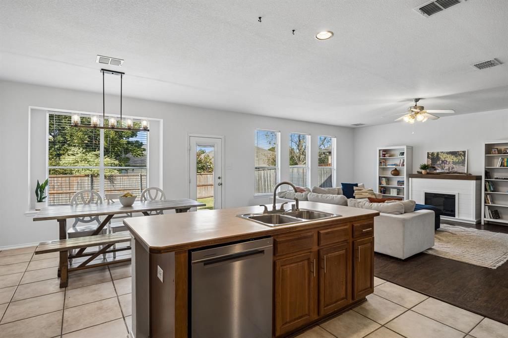 Enjoy the versatility of this open-concept kitchen and dining area, designed to bring functionality and connection together. The kitchen features abundant wood cabinetry, expansive counter space, a built-in dishwasher, and a convenient center island with an integrated sink. Natural light pours through multiple windows, illuminating the dining area and adjoining living room. Tile flooring in the kitchen and dining space transitions beautifully to wood-look flooring in the living area, creating distinct yet connected spaces.