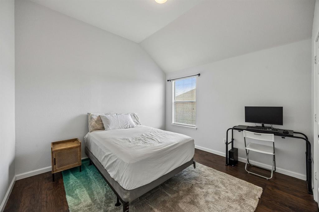 A bright and welcoming secondary bedroom featuring a vaulted ceiling, neutral walls, and rich wood-look flooring. The window brings in natural light, while the generous wall space offers flexibility for a variety of layouts and uses. Its clean, understated finishes create a versatile backdrop ready to complement a range of decorating styles.