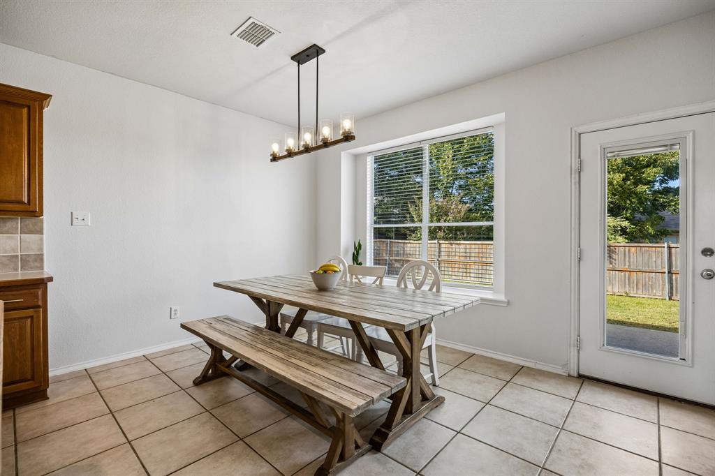 Bright and inviting, the dining area features a large window with backyard views and a glass-paneled exterior door that provides convenient access to the outdoor space. Neutral tile flooring extends throughout the area, offering both practicality and a cohesive look. A modern linear chandelier adds character overhead, while the open connection to the kitchen makes serving meals and entertaining guests a breeze.