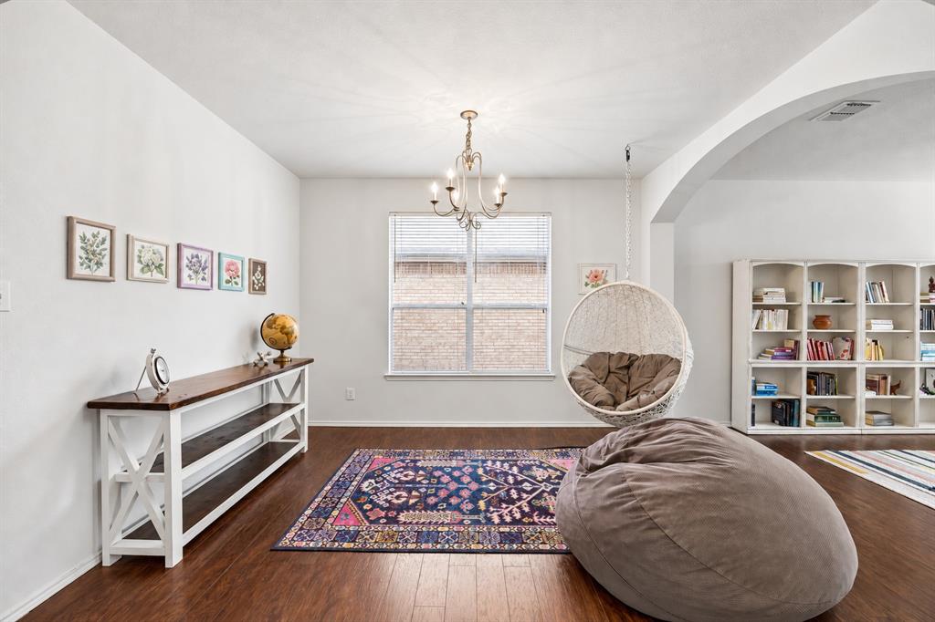 The formal dining room is currently being used as a versatile secondary living space. Crisp white walls, rich wood flooring, and an elegant chandelier create a bright, inviting atmosphere, while a graceful arched opening adds architectural character and connects the space to the adjoining office space or formal living space.