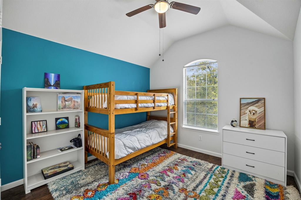 Enjoy the character and charm of this bedroom, featuring a vaulted ceiling, bold turquoise accent wall, and a beautiful arched-top window that allows natural light to filter inside. Rich wood-look flooring and crisp white trim complement the colorful walls, while the spacious layout provides flexibility for a variety of bedroom arrangements and personal touches.