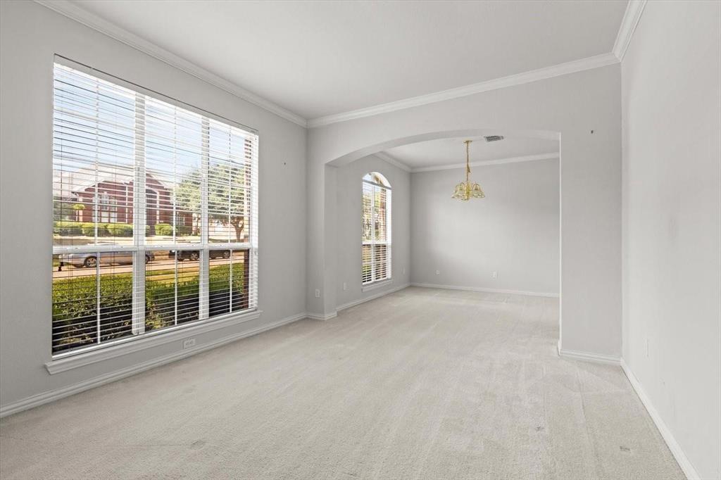 Neutral interior space featuring arched architectural detailing, crown molding, expansive windows, wall-to-wall carpeting, and a multi-arm chandelier