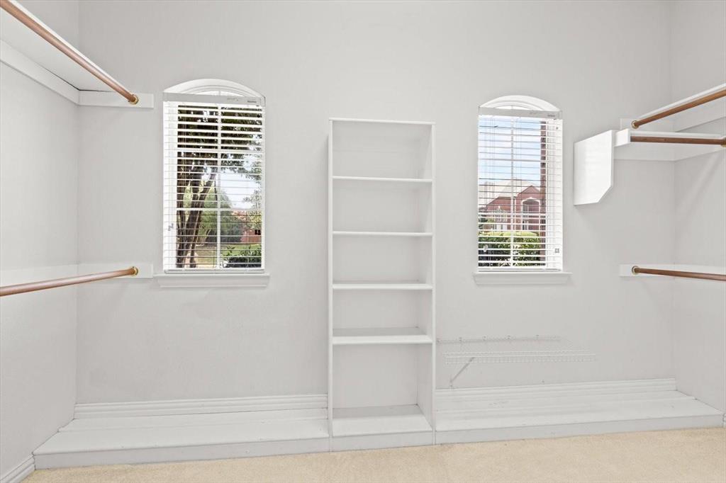 Walk-in closet featuring dual arched windows, built-in shelving, white integrated cabinetry, and metal hanging rods
