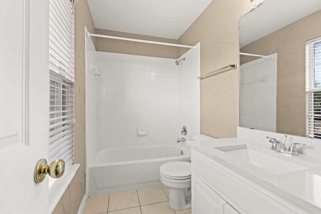 Bathroom featuring a vanity with a countertop, integrated basin, and polished chrome faucet, alongside a tub-shower combination with tile surround and tile flooring