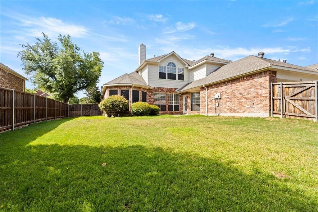 Rear exterior featuring a brick and siding facade, expansive lawn, mature landscaping, and wood privacy fencing