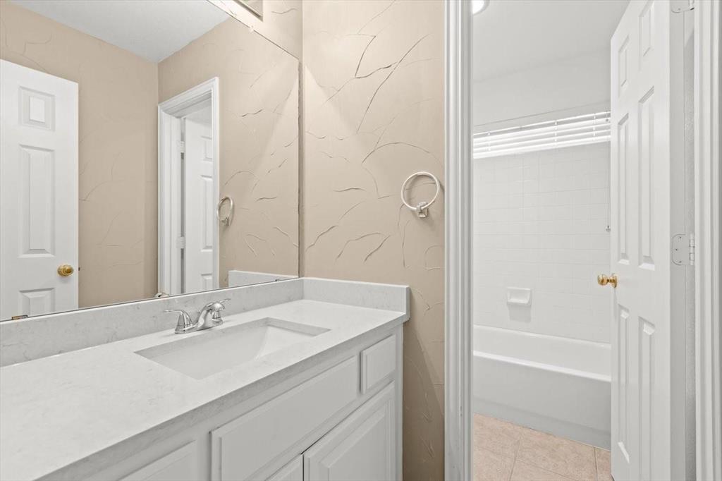 White vanity with stone-style countertop and integrated sink, large wall-mounted mirror, and tile-surround shower and tub combination