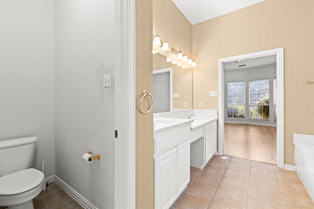Bathroom featuring a dual-sink vanity with white cabinetry, ceramic tile flooring, a large wall-mounted mirror, and multi-bulb overhead lighting