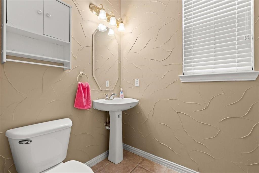Pedestal sink, wall-mounted storage cabinetry, octagonal vanity mirror, multi-light fixture, and textured wall finish