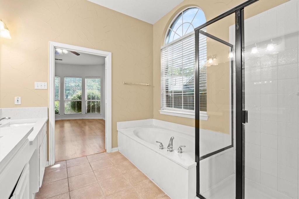 Bathroom featuring a soaking tub, arched window, walk-in shower with a black frame, double-sink vanity with solid-surface countertop, and tile flooring