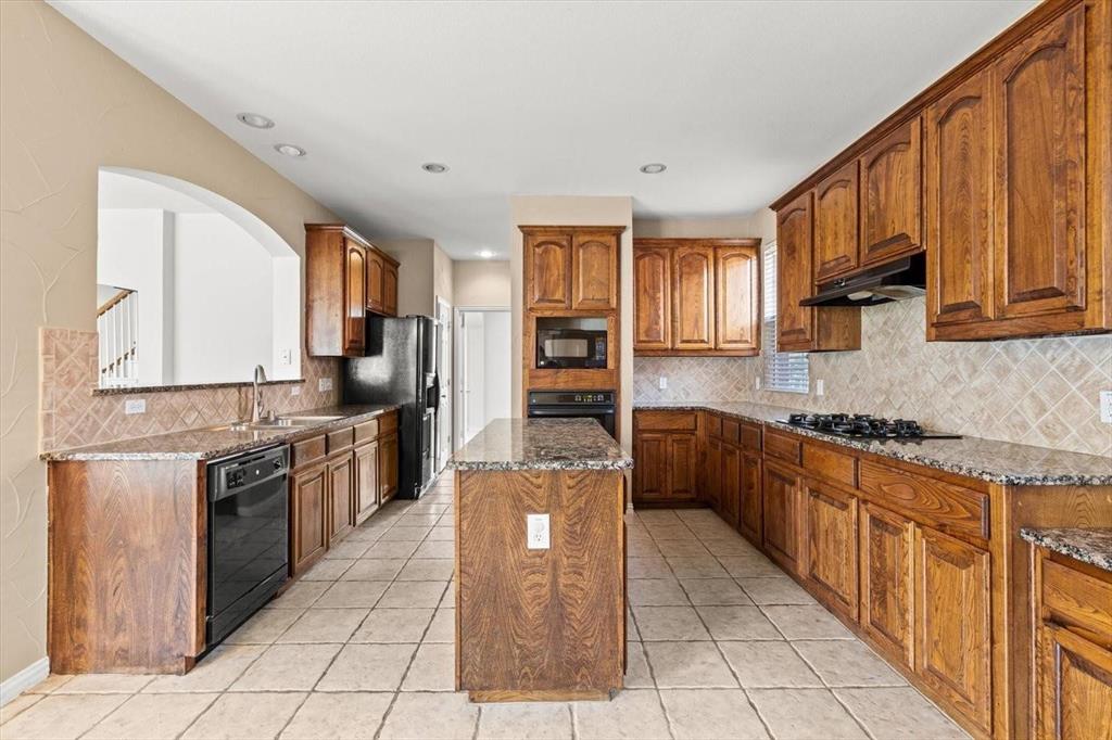 Kitchen featuring wood cabinetry, stone countertops, central island, tile backsplash, and recessed lighting