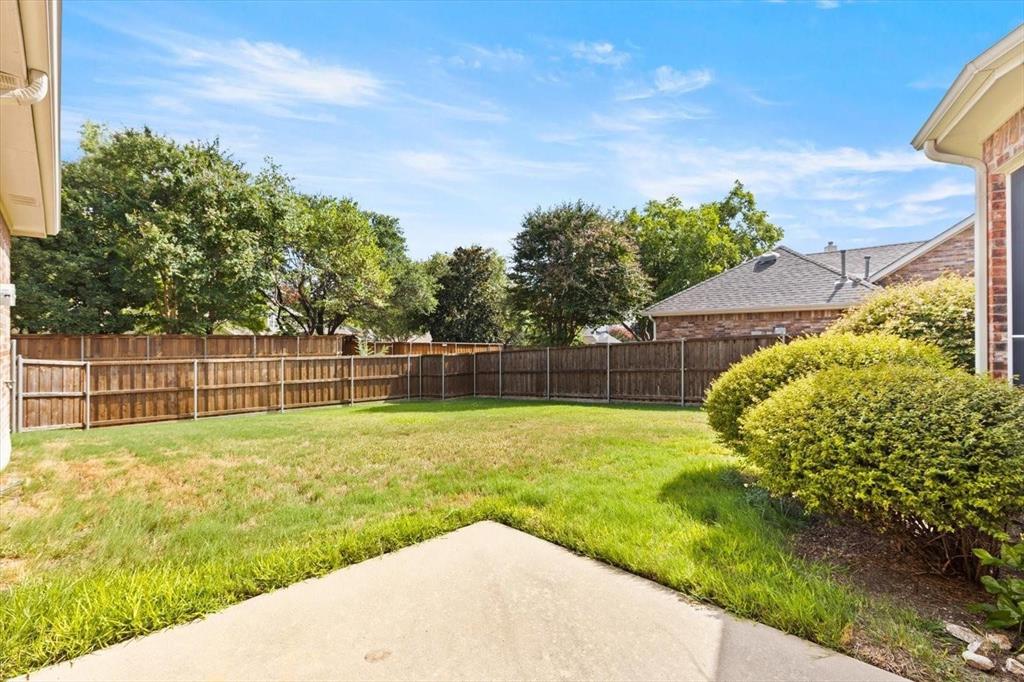 Rear exterior area featuring a concrete patio, wood privacy fencing, a manicured lawn, and mature landscaping